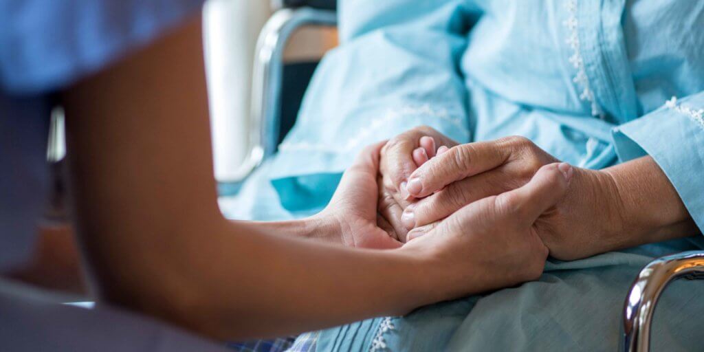 A nurse holds the hand of a patient who as a Kennedy terminal ulcer.