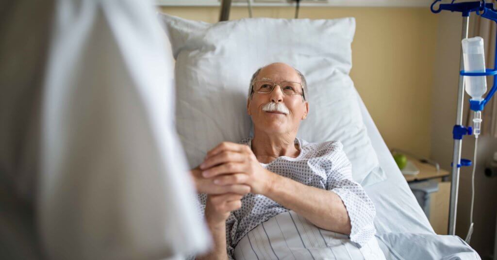 A senior patient holds a nurses' hand in the ICU.