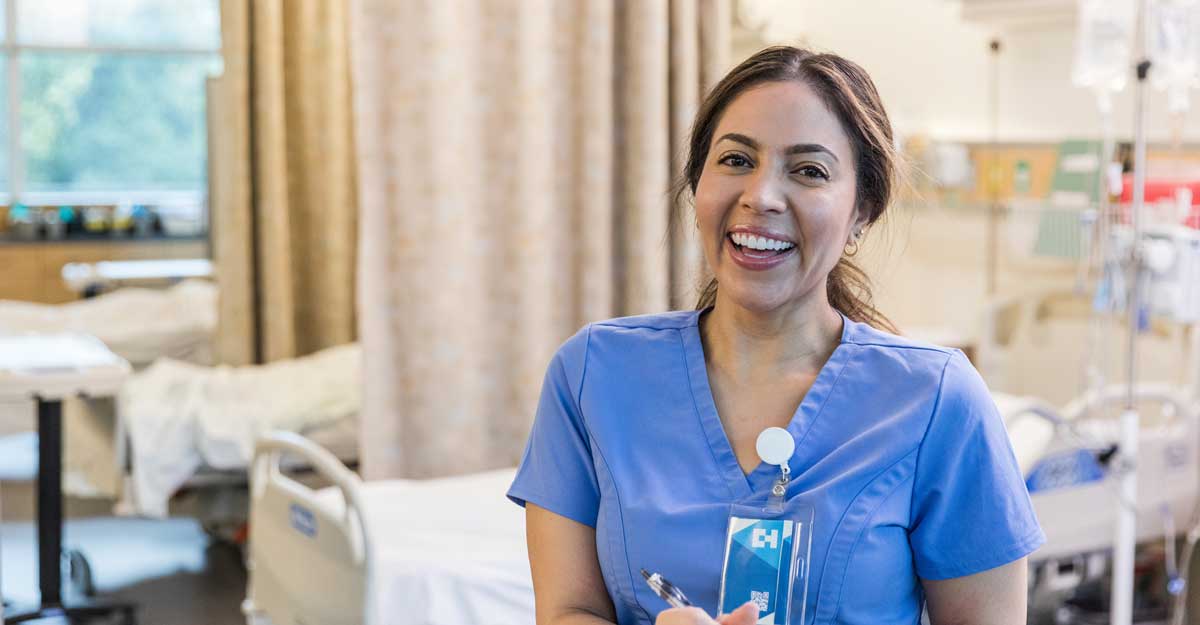 nurse sits and smiles in hospital room with pen and clipboard